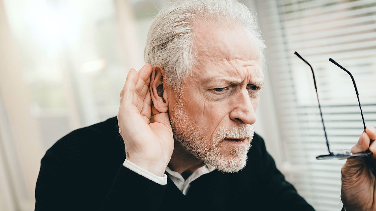 Man with hearing loss holding his glasses with a struggling look on his face